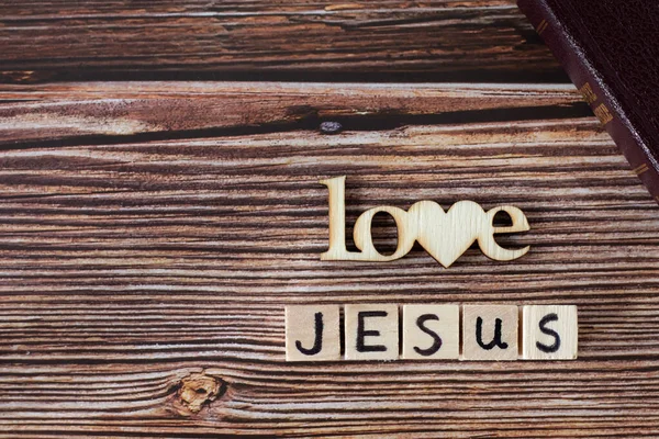 Love Jesus text written with wooden cubes and letters with heart shape placed on rustic background with closed Holy Bible Book. Copy space. Top view. Christian biblical concept.