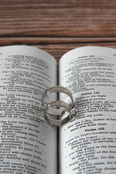 Two wedding rings on open Holy Bible Book placed on wooden background. Vertical shot, a closeup. Christian biblical concept of marriage, love, faithful relationship, covenant before God Jesus Christ.