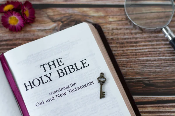 Holy Bible Book with ancient key and magnifying glass on wooden background. Top view. Christian study of old and new testament Scripture, wisdom, prophecy, and revelation from God Jesus Christ.