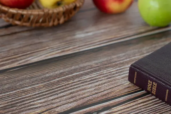 Closed Holy Bible Book and apples in various colors on a rustic wooden table with copy space.