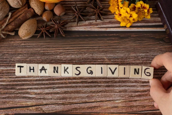 Thanksgiving word written on wooden cubes with handwritten letters on wooden background with autumn still life and Holy Bible Book. Top table view.