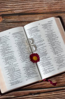 Çiçekli kutsal bir İncil 'in üzerinde iki alyans. Dikey çekim, üst masa görüntüsü. Hıristiyan aşkı, bağlılık, evlilik ve bağlanma ilişkisi incilsel kavram.