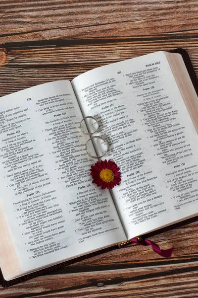Two wedding rings on an open holy bible book with flower. Vertical shot, top table view. Christian love, commitment, marriage, and bonding relationship biblical concept.