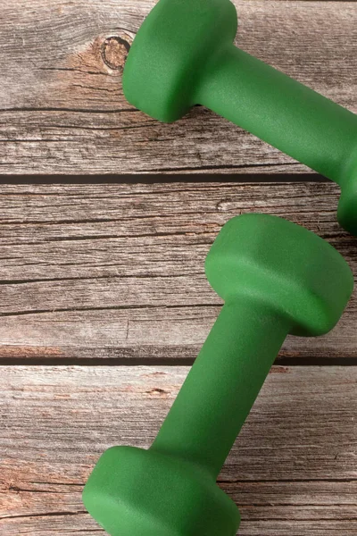 Green dumbbells on wooden background. Vertical shot, top view. A close-up. Weight lifting, building muscle strength, training and exercising concepts.