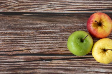 Tahta masada üç elma (kırmızı, yeşil ve sarı). Üst Manzara. Uzayı kopyala Farklı renklerde taze organik sonbahar meyveleri.