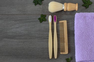 Tahta diş fırçaları, bambu tarak, tıraş fırçası ve ahşap masa üzerinde yeşil yapraklı banyo havlusu. Uzayı kopyala, üst görünüm. Çevre dostu ve sürdürülebilir hijyen ürünleri, plastiksiz konsept.