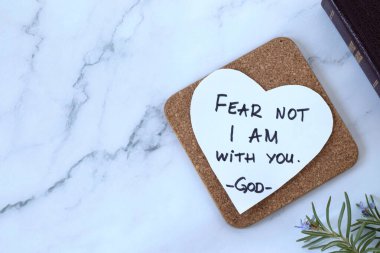 Fear not, I am with you, handwritten verse on heart-shaped note and closed holy bible book. Top table view. Copy space. Words of encouragement and hope from God Jesus Christ, Isaiah 41:10.