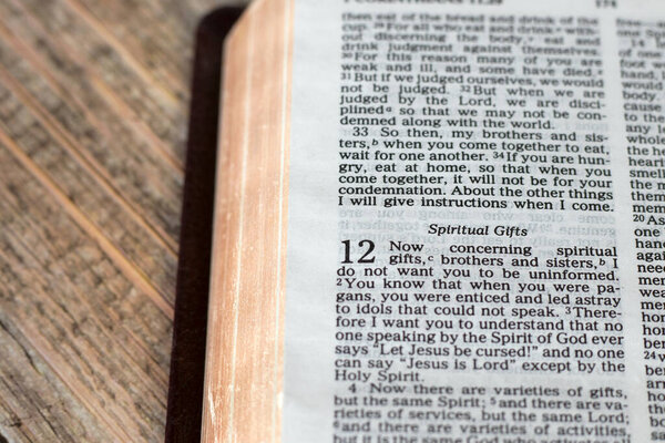 Христианские стихи о духовных дарах в открытой священной библейской книге с золотыми страницами на деревянном столе. Крупный план.