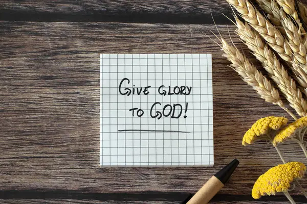 Give glory to God, handwritten Christian quote with pen, ripe wheat ears and flowers on wooden table. Top view. Praise, worship, thanksgiving, and blessing LORD Jesus Christ, biblical concept.