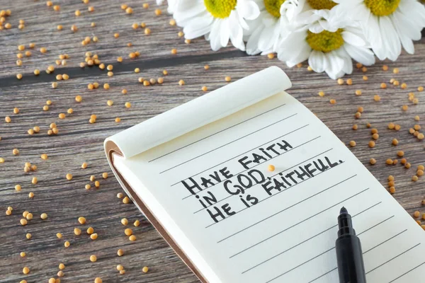 Have faith in God, He is Faithful. Inspiring Christian bible quote handwritten in notebook with mustard seed and flowers on wooden table. Biblical promise, peace, trust, and belief in Jesus Christ.