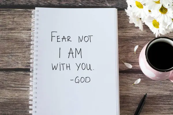 Fear not I am with you, God. Handwritten text in notebook with flowers and cup of coffee on wooden table. Inspiring bible verse. Christian concept of comfort, peace, and love of Jesus Christ. Top view.