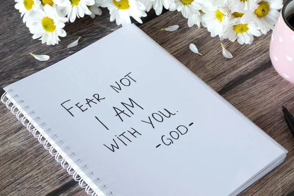 Fear not I am with you, God. Handwritten text in notebook with flowers and cup of coffee on wooden table. Inspiring bible verse. Christian concept of comfort, peace, and love of Jesus Christ.