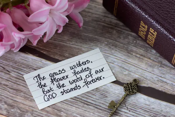 Grass withers, flower fades, but the Word of our God stands forever, handwritten text with holy bible and ancient key on wood. Jesus Christ\'s eternal power, wisdom, truth, Christian biblical concept.