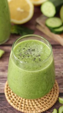 Chia tohumları yeşil detoks smoothie üzerine düşüyor. Tahta masada bambu kamışla taze meyve ve sebzeyle. Dikey video. Yakın plan. Sağlıklı karışımlı içecek, sürdürülebilirlik kavramı.