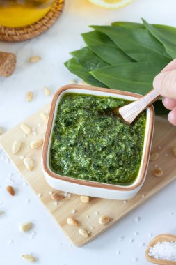 Çam fıstıklı yabani sarımsak pesto, zeytin yağı ve tahtanın üzerinde bir demet taze Ramson yaprağı (ayı pırasa). Üst masa manzaralı. Sağlıklı yeşil sos, organik gıda konsepti.