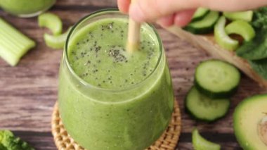 Yeşil detoks smoothie ile Chia tohumları, salatalık, kereviz, ıspanak ve avokadoyu bambu kamışıyla karıştırıyorum. Yakın plan. Sağlıklı karışım, organik meyve suyu, sürdürülebilirlik kavramı.