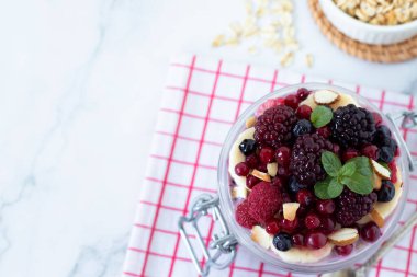Beyaz mermer masada kavanozda meyveli ve yulaf ezmeli kahvaltı. Üst Manzara. Uzayı kopyala Yakın plan. Temiz organik sabah yemeği, bitkisel gıda konsepti yemek..