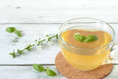 Tahta masanın üzerinde cam bardakta taze fesleğen çayı. Sarı renkli sıcak bitkisel içecek. Yakın plan. Seçici odaklanma. Boşluğu kopyala.