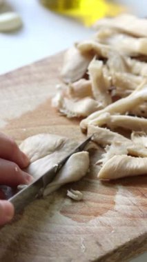 Female hand slicing oyster mushrooms on rustic wooden cutting board. Close-up. Vertical video. Preparation of organic plant-based food ingredient for healthy homemade meal.