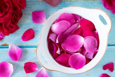 Kırsal ahşap masadaki su içinde pembe ve kırmızı gül yaprakları. Üst Manzara. Kapatın. Aromaterapi, sağlık, kaplıca, cilt bakımı, doğal organik temel yağ veya parfüm konseptinin hazırlanması.