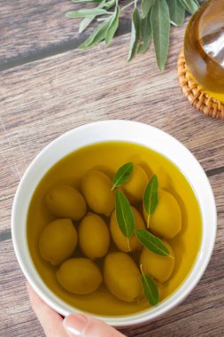 Elde tutulan yeşil zeytin kabı ve ekstra saf zeytin yağı ile ahşap masada. Üst Manzara. Sağlıklı yağ yemek, Akdeniz gıda kavramı.