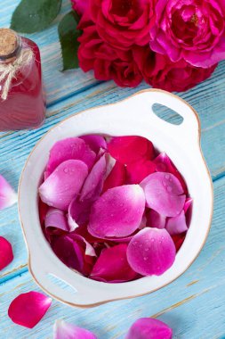 Kasede gül yaprakları, su, buket ve ahşap masa üzerinde gerekli yağ şişesi. Üst Manzara. Aromaterapi, sağlık, kaplıca, cilt bakımı ve çiçek parfümü konsepti..