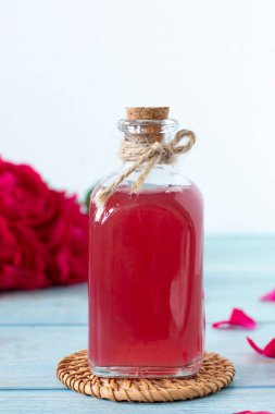 Cam şişede kırmızı gül suyu, beyaz arka planda tahta üzerinde çiçekler ve yapraklar. Yakın plan. Uzayı kopyala Doğal yağ, organik parfüm, aromaterapi, cilt bakımı konsepti.