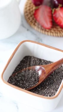 Çiğ organik chia tohumları tahta kaşıkla bir kaseye düşüyor. Dikey video. Yakın plan..