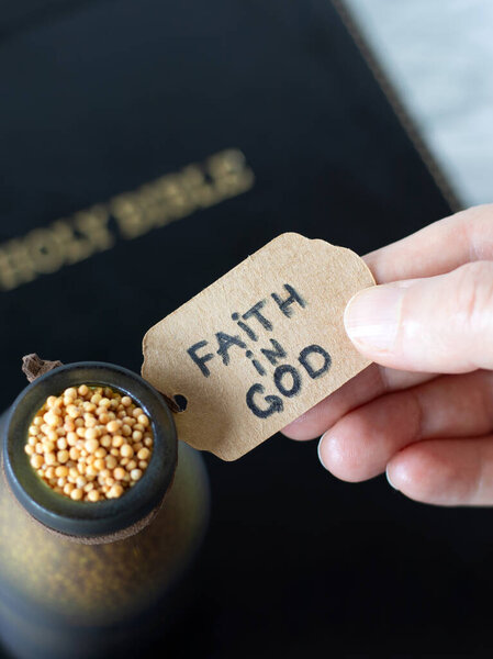 Hand-holding handwritten note: Faith in God on a bottle with mustard seeds and holy bible book in the background. Top view. Trust and belief in Jesus Christ, Christian biblical concept.