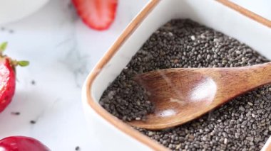 Chia tohumları tahta kaşıkla bir kaseye düşüyor. Yakın plan. Üst Manzara. Sağlıklı ev yapımı kahvaltı hazırlığı.