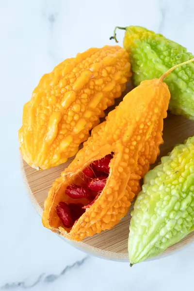 stock image Ripe karela (bitter melon, Momordica charantia) with orange and green color isolated on white marble background. Close-up. Top table view. Organic fresh tropical fruit.