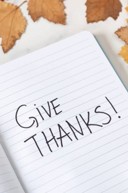 Give thanks, handwriting in notebook with autumn leaves on white background. Close-up. Thanksgiving and gratitude concept. clipart