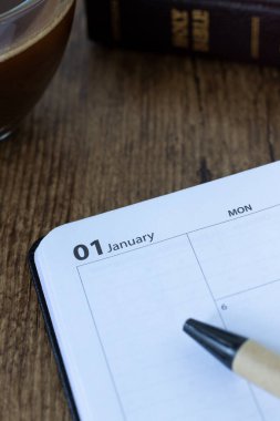 1 Ocak takvim defterinde bir fincan kahve ve kutsal İncil var. Yakın plan. Hıristiyan çalışma planlayıcısı, okuma organizatörü, İncil konsepti.