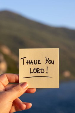 Elle yazılmış bir not: Arka planda dağ ve nehir suyu olan teşekkürler Tanrım. Yakın plan. İncil 'de geçen şükran ve şükran kavramını Tanrı' ya borçluyuz..