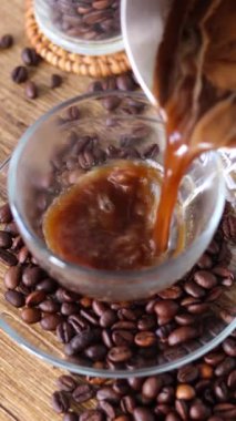 Kırsal ahşap masada kahve çekirdekleri olan cam bir fincana sıcak kahve dökmek. Dikey video. Yakın plan..