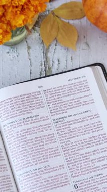 Hıristiyanlık incili, açık kutsal kitapta balkabağı ve sonbahar yapraklarıyla ahşap masada. Dikey video. Üst Manzara. Yeni Ahit Kutsal Kitabı 'nı okumak, İncil' deki kavram..