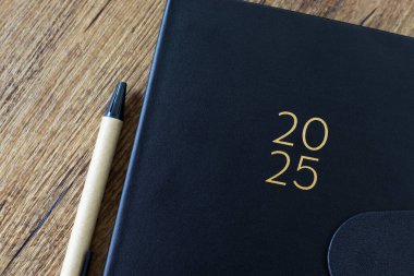 2025 yılbaşı not defteri ve tahta masa üzerinde kalem. Üst Manzara. Takvim planlayıcısı, yıllık organizatör, iş etkinliği takvimi kavramı.