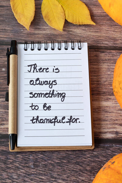 Вдохновляющая рукописная благодарственная цитата в блокноте с тыквой и сушеными осенними листьями на деревянном фоне. Вид сверху.