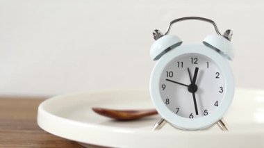 Boş tabakta çalar saat ve beyaz arka planda tahta kaşık. Aralıklı oruç ve yemek planlama konsepti. Yakın plan..