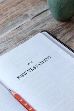 İncil 'in açık sayfasında, üzerinde kahve fincanı olan ahşap bir masa. Yakın plan. Tanrı 'nın İncili' ni, Hristiyan İncili kavramını okuyorum..