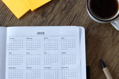 2025 takvim yılı, defter planlayıcısı, ahşap masa üzerinde kahve fincanı ve yapışkan notlarla. Üst Manzara. Yıllık hedefler, bütçe, hedefler, aylık takvim kavramı.