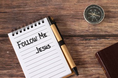 Follow Me, Jesus, handwritten quote in notebook with compass and holy bible book on wooden background. Top view. Christian direction, obedience, guidance, and faith, biblical concept. clipart