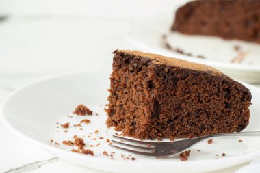 Beyaz arkaplanlı çikolatalı kek dilimi. Yakın plan. Seçici odaklanma. Uzayı kopyala Ev yapımı vejetaryen tatlı, kakao ve keçiboynuzu tozu..