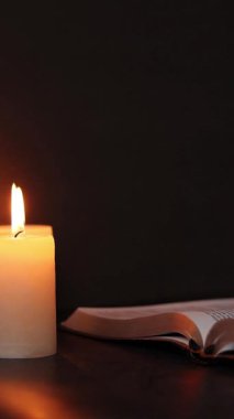 Karanlıkta yanan mumlarla kutsal İncil 'i okumak. Dikey video. İncil 'deki bilgelik, kehanet ve Tanrı' ya olan inanç kavramı..