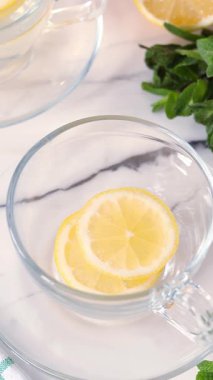 Taze limon dilimlerinin üzerine ev yapımı nane çayı döküyorum. Dikey video. Yakın plan..