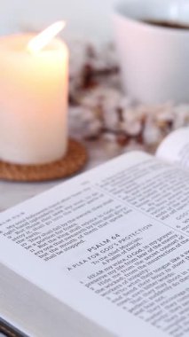 Evde mum ve bir fincan kahveyle açık kutsal İncil 'den ders çalışıyorum. Dikey video. Seçici odaklanma. Eski Ahit 'i okumak, İncil' deki Hristiyan kavramını okumak.