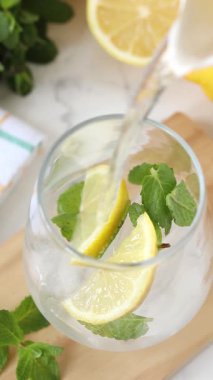 Buzlu bir bardakta taze nane ve limon üzerine soğuk su dökmek. Dikey video. Ev yapımı limonata hazırlığı.
