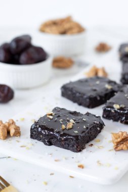 Çikolatalı kek, yanında hurma ve beyaz tabakta ceviz. Sağlıklı vejetaryen çiğ tatlı..