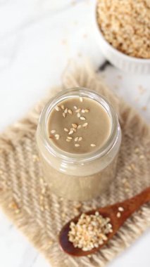 Kavrulmuş susam tohumları tahini dolu bir kavanoza dökülüyor. Dikey video. Üst görünüm.