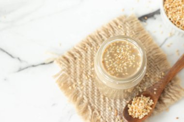 Tahini kavrulmuş susam tohumlarıyla beyaz mermer masada bir kavanozda. Üst Manzara. Boşluğu kopyala.